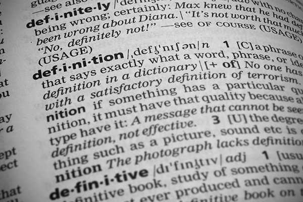 Closeup shot of the word definition in a dictionary. Page curves and has a vignetting or edge burn effect where the corners are darker. Focus is on the word definition.