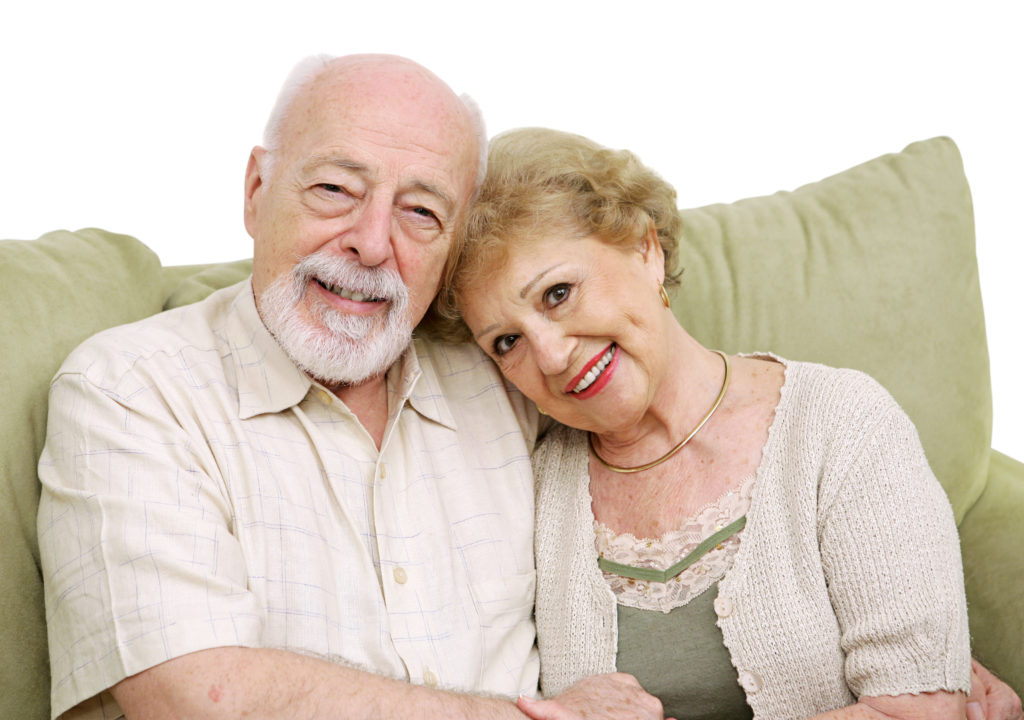 An attractive senior couple at home on the couch together. Isolated on white.